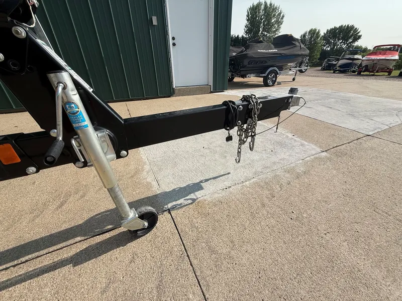Slide: The Image of A boat trailer with a jack wheel and safety chains on a concrete surface near a building. - 28