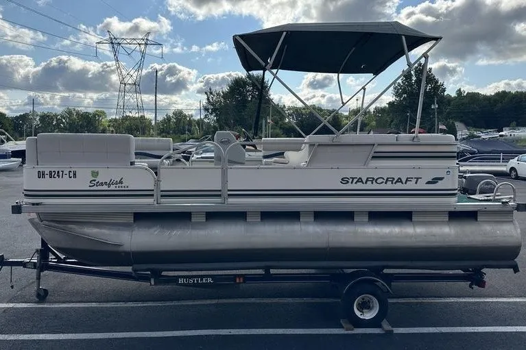 Slide: The Image of 1999 Starcraft Starfish 180 pontoon boat on trailer, parked outdoors under cloudy sky. - 8