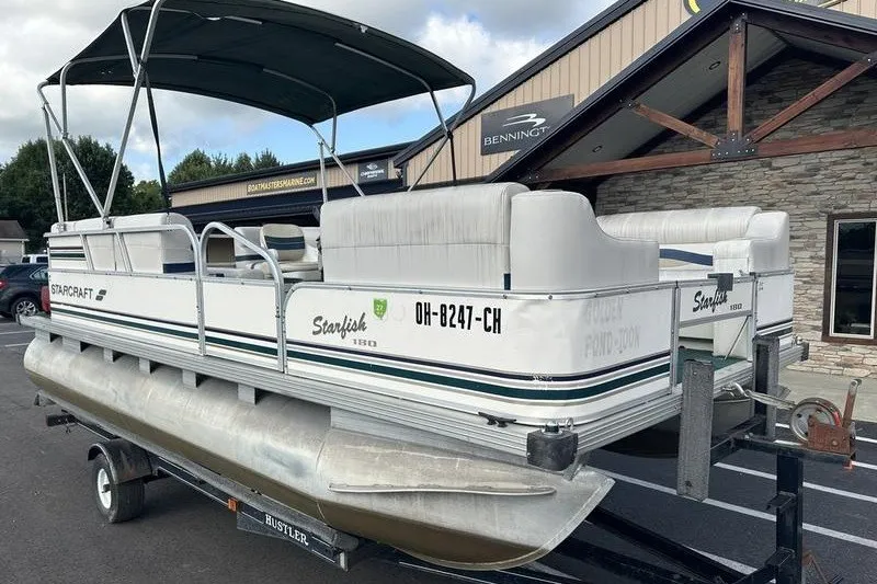 Slide: The Image of 1999 Starcraft Starfish 180 pontoon boat on trailer, parked outside a building. - 2