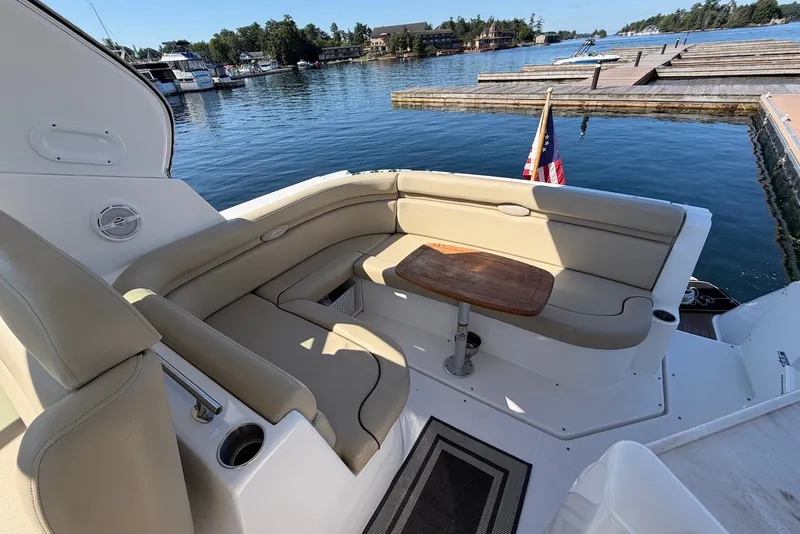 Slide: The Image of 2015 Rinker 340 Express Cruiser interior with seating and table, docked by a scenic waterfront. - 15