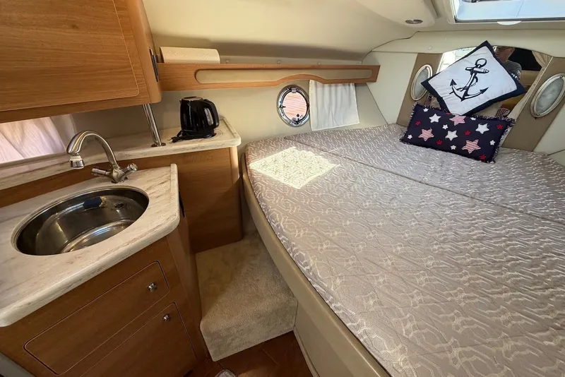 Slide: The Image of 2015 Rinker 340 Express Cruiser cabin with bed, sink, and nautical-themed decor. - 31