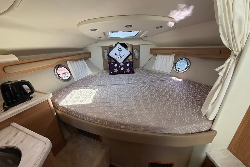 Slide: The Image of 2015 Rinker 340 Express Cruiser cabin interior with bed, portholes, and kettle. - 30