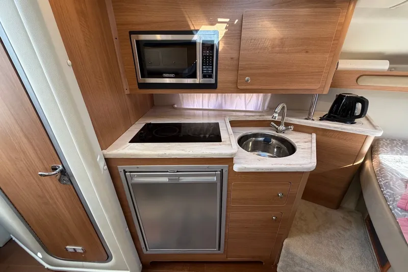 Slide: The Image of Compact kitchen in 2015 Rinker 340 Express Cruiser with microwave, sink, and stovetop. - 29