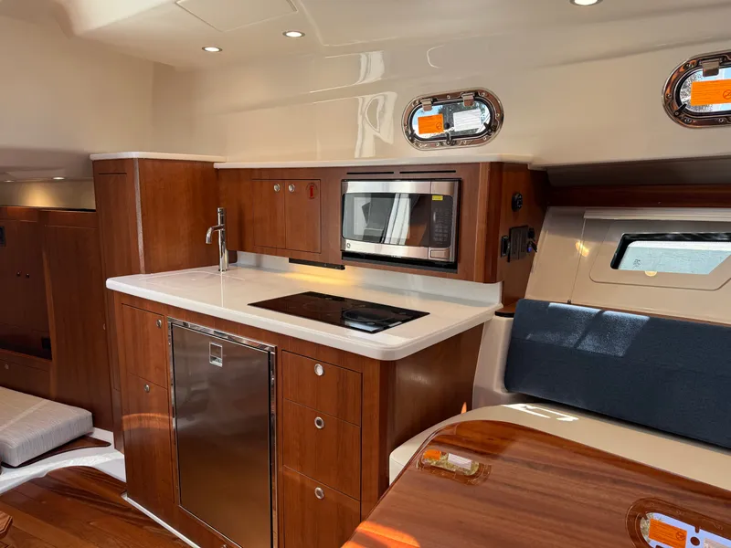 Slide: The Image of The 2027 Pursuit OS 355 Offshore galley features wood cabinets, a microwave, and a cooktop. - 30
