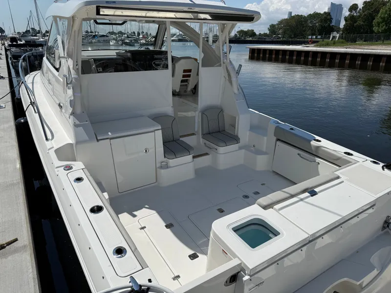 Slide: The Image of The 2027 Pursuit OS 355 Offshore is docked in a calm harbor. It features a spacious, white deck. - 7