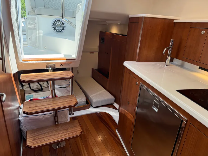 Slide: The Image of Interior of a Pursuit OS 355 Offshore with wooden floors, stairs, and a small kitchenette. - 36