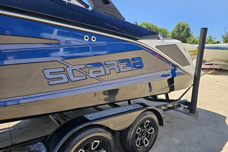 Slide: The Image of 2022 Scarab 255 Wake ID boat on trailer, featuring sleek blue and black design. - 24