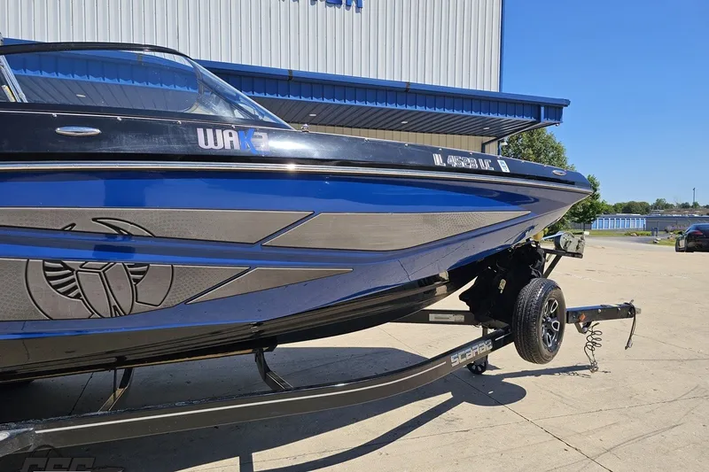 Slide: The Image of 2022 Scarab 255 Wake ID boat on trailer, blue and black design, parked outdoors. - 5