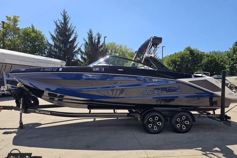 Slide: The Image of 2022 Scarab 255 Wake ID boat on trailer, sleek design, blue and black color scheme. - 21
