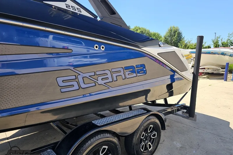 Slide: The Image of 2022 Scarab 255 Wake ID boat on trailer, featuring sleek blue and black design. - 22