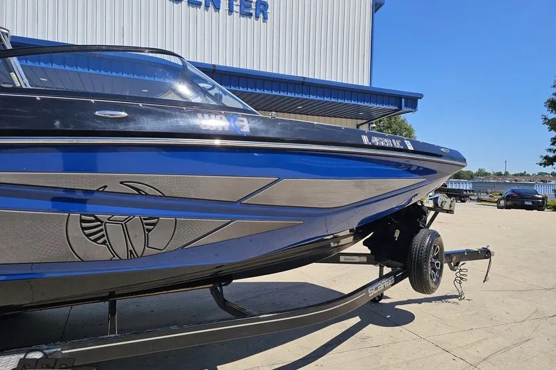 Slide: The Image of 2022 Scarab 255 Wake ID boat on trailer, blue and black design, parked outside. - 12