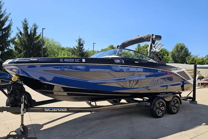 Slide: The Image of 2022 Scarab 255 Wake ID boat on trailer, blue and black design, parked outdoors. - 20