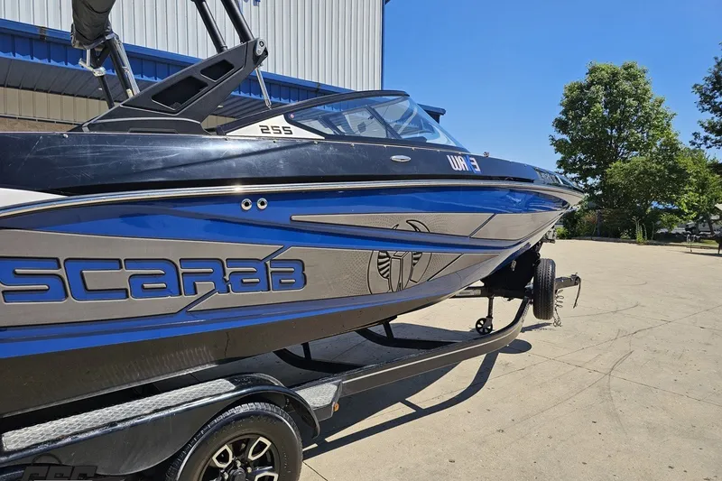 Slide: The Image of 2022 Scarab 255 Wake ID boat on trailer, parked outdoors under clear blue sky. - 9