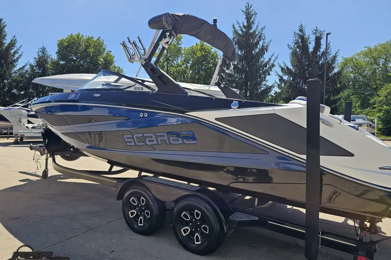 Slide: The Image of 2022 Scarab 255 Wake ID boat on trailer, parked outdoors, with trees in background. - 28