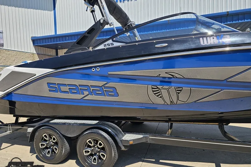 Slide: The Image of 2022 Scarab 255 Wake ID boat on trailer, blue and black design, parked outdoors. - 6