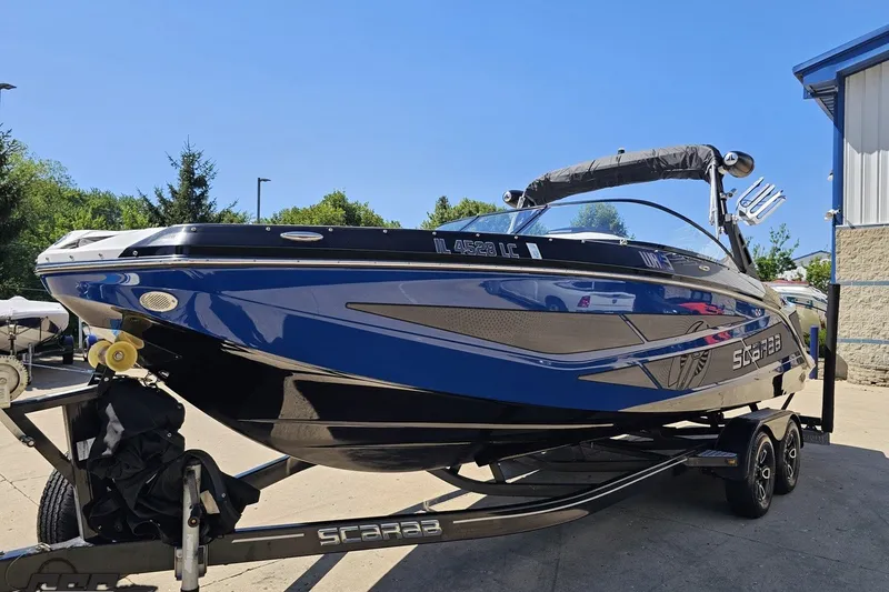 Slide: The Image of 2022 Scarab 255 Wake ID boat on trailer, blue and black design, parked outdoors. - 19