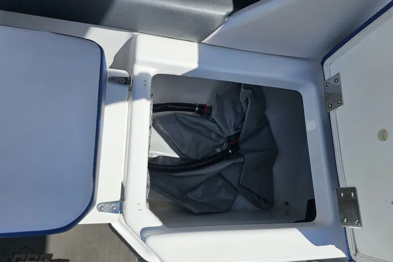 Slide: The Image of Open storage compartment in a 2022 Scarab 255 Wake ID boat, showing interior hoses. - 54