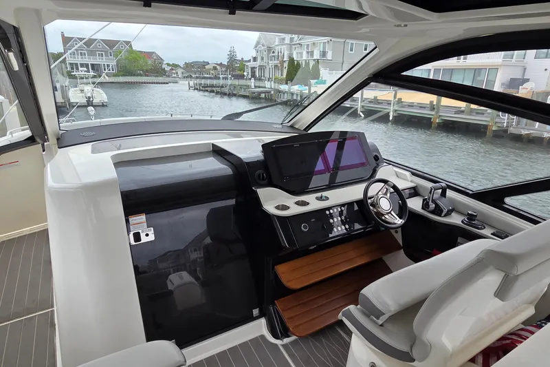 Slide: The Image of 2023 Sea Ray Sundancer 370 Outboard helm with modern controls, overlooking waterfront homes. - 2