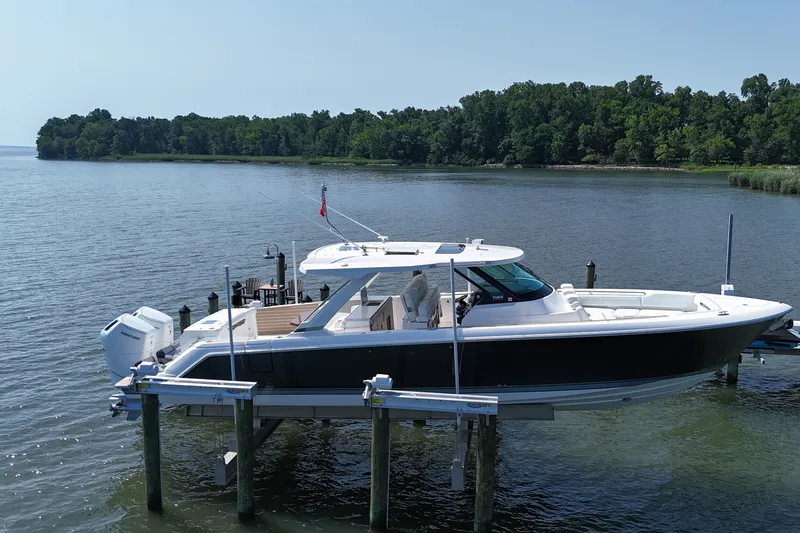 The Image of 2025 Tiara Yachts 43 LS on lift, docked by a serene, wooded shoreline. - 0