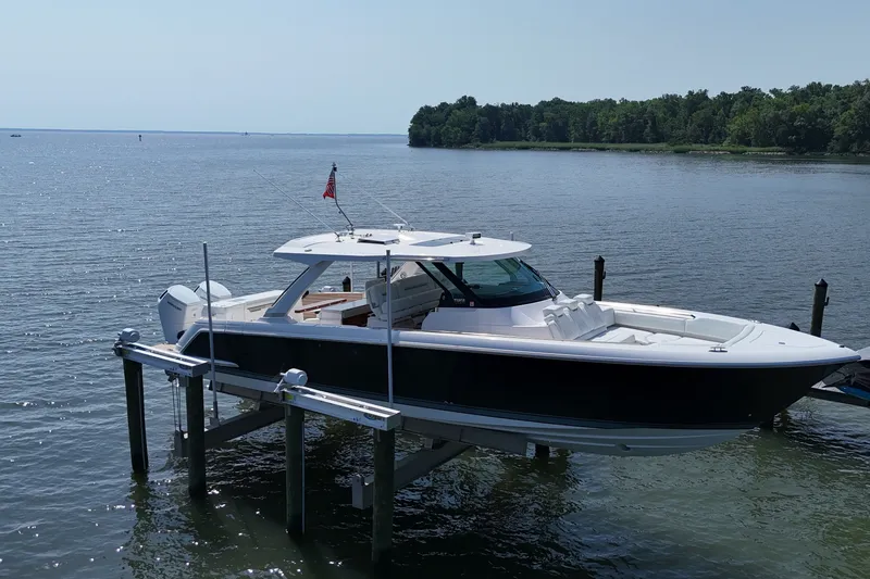 Slide: The Image of 2025 Tiara Yachts 43 LS on lift, docked by serene waters, with lush green shoreline. - 1