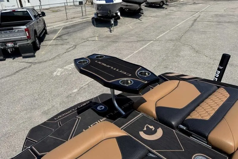 Slide: The Image of 2025 Centurion Ri245 boat interior with stylish seating and cup holders in a parking lot. - 1