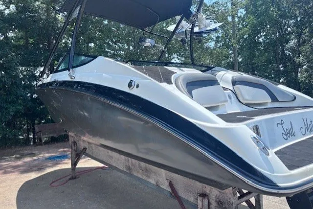 Slide: The Image of 2013 Yamaha Boats 212X on a stand, featuring sleek design and canopy, surrounded by trees. - 2