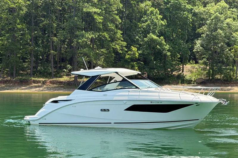 Slide: The Image of 2025 Sea Ray Sundancer 320 yacht on serene lake with lush forest backdrop. - 16
