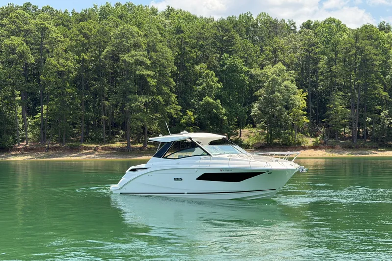 Slide: The Image of 2025 Sea Ray Sundancer 320 cruising on a serene lake with forested shoreline. - 15