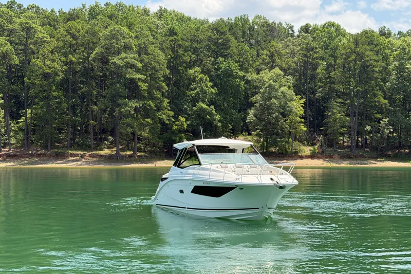 Slide: The Image of 2025 Sea Ray Sundancer 320 cruising on a serene lake with forested shoreline. - 14