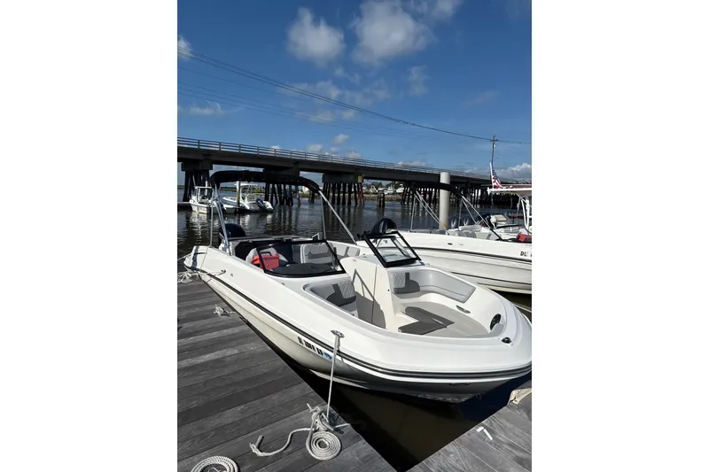 Slide: The Image of 2023 Bayliner VR6 Bowrider OB docked near a bridge under a clear blue sky. - 2