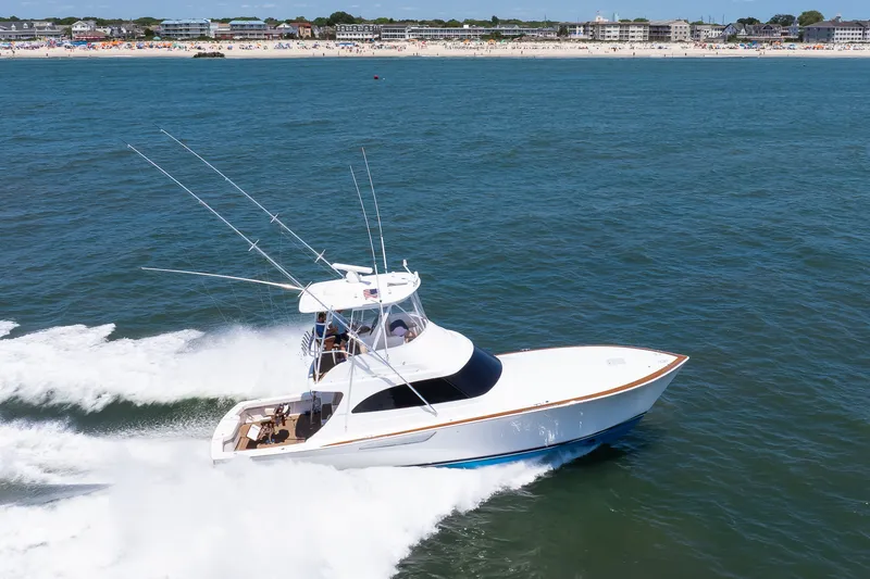 Slide: The Image of 2021 Viking 46 Billfish yacht cruising on open water near a busy shoreline. - 26