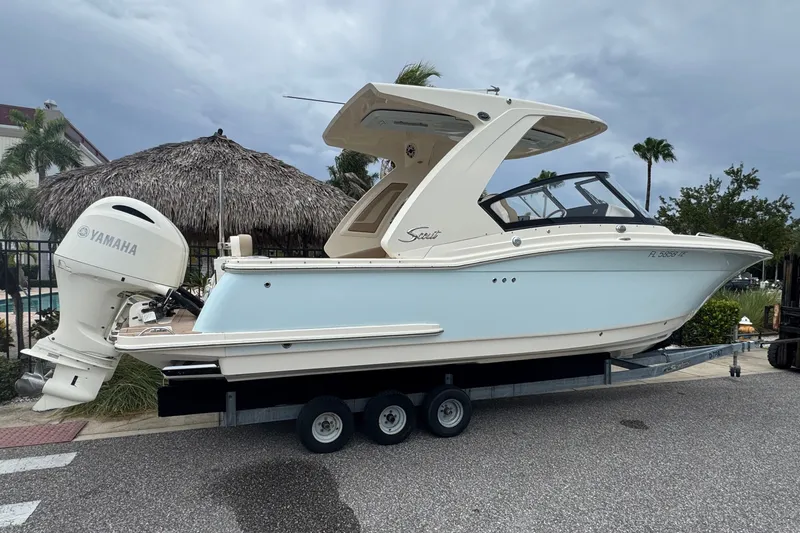 Slide: The Image of 2022 Scout 277 Dorado boat on trailer with Yamaha engine, parked near tropical setting. - 2