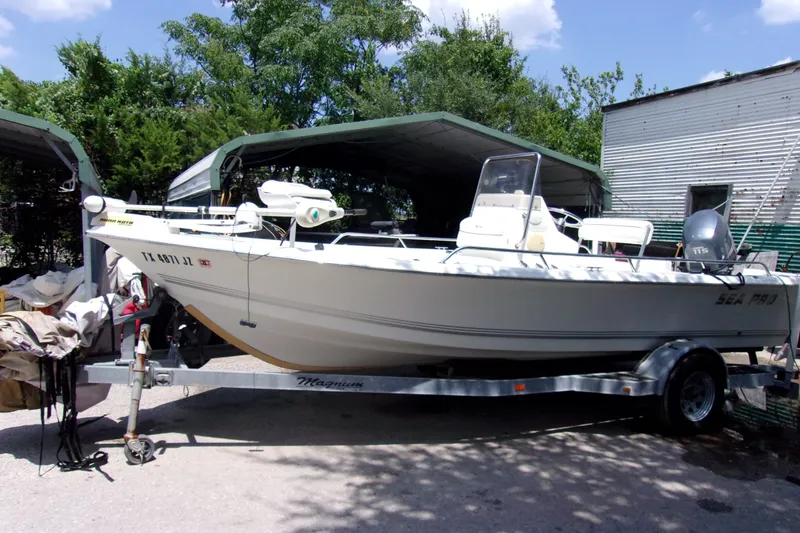 The Image of 2004 Sea Pro SV1900CC Bay Boat on trailer, parked outdoors under a metal canopy. - 1