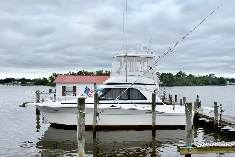 The Image of 1997 Riviera 34 Convertible yacht docked by a serene waterfront under cloudy skies. - 0