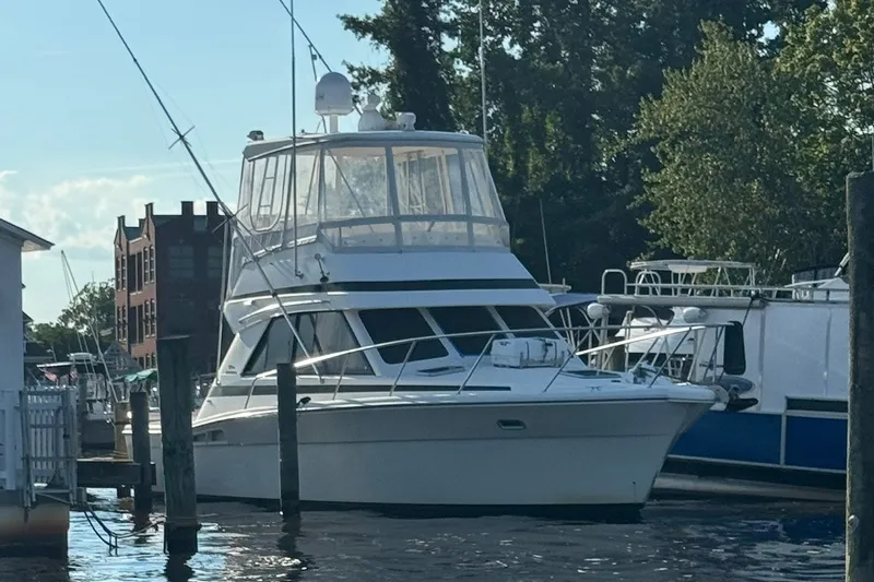 Slide: The Image of 1997 Riviera 34 Convertible yacht docked at marina, surrounded by trees and buildings. - 4