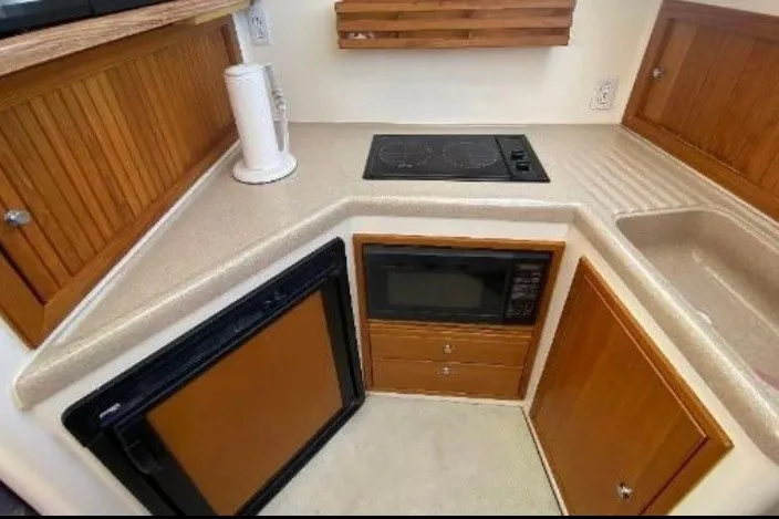 Slide: The Image of Compact kitchen area in a 1997 Riviera 34 Convertible boat with stove, microwave, and fridge. - 38