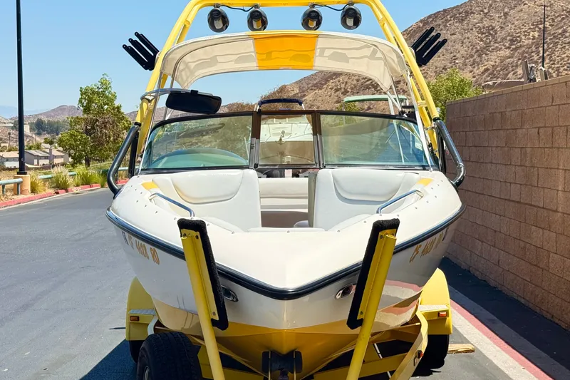 Slide: The Image of 2003 Centurion Cyclone C4 boat on trailer, parked near a brick wall and scenic hills. - 2