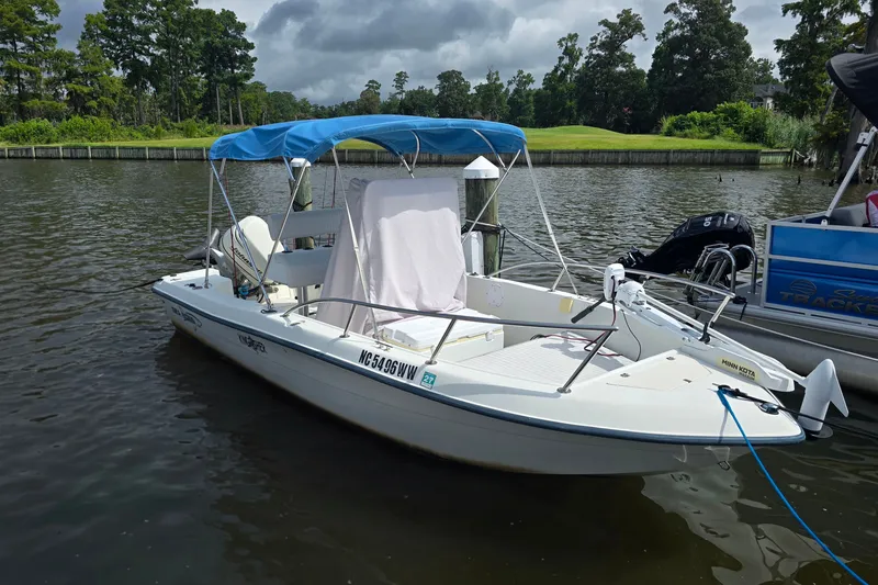 The Image of 2004 Sea Boss 180 Center Console boat docked on a calm river with lush greenery. - 1
