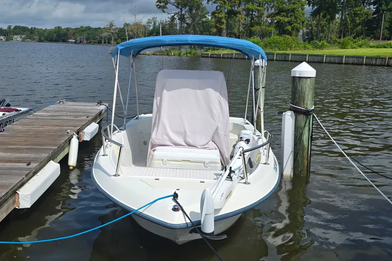 Slide: The Image of 2004 Sea Boss 180 Center Console boat docked by a serene lake with lush greenery. - 2