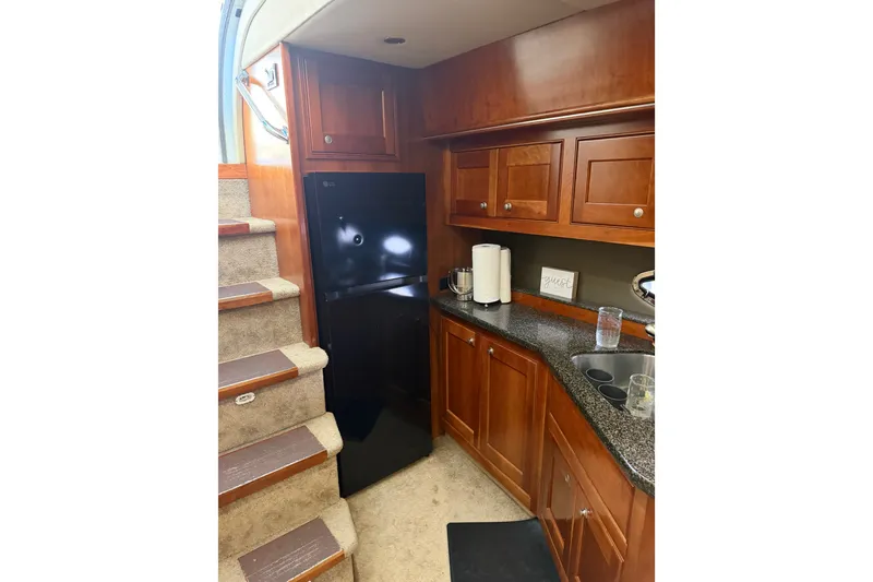 Slide: The Image of 2006 Cruisers Yachts 560 Express interior kitchen with wooden cabinets and black refrigerator. - 11
