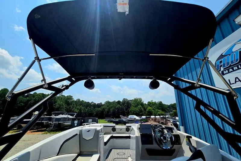 Slide: The Image of 2024 Starcraft SVX 231 OB boat interior with canopy, steering wheel, and seating, under sunny sky. - 52