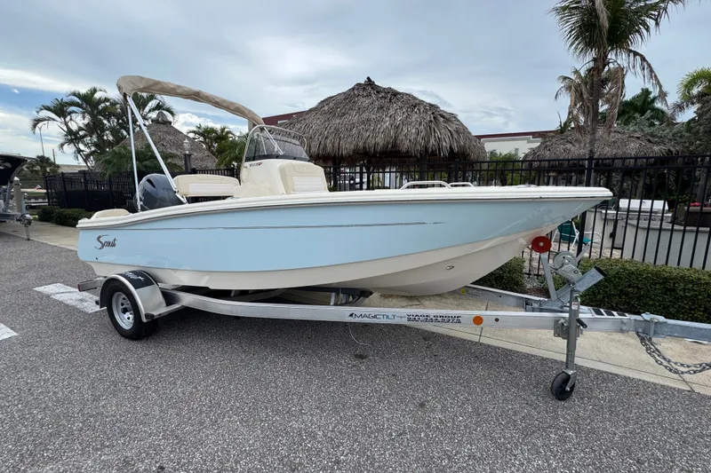 Slide: The Image of 2027 Scout 188 Sportfish boat on trailer, parked outdoors near tropical foliage. - 1