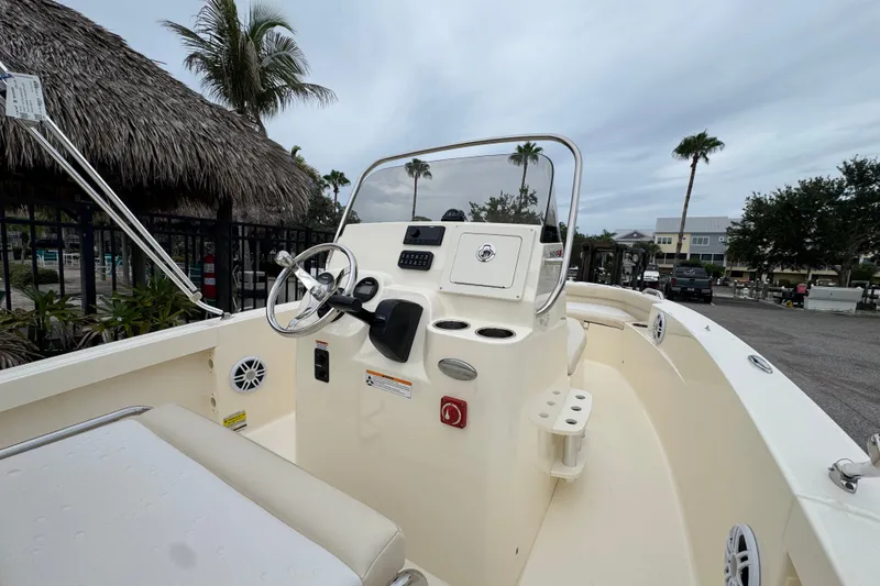 Slide: The Image of 2027 Scout 188 Sportfish boat interior with steering wheel and console, docked under cloudy skies. - 8