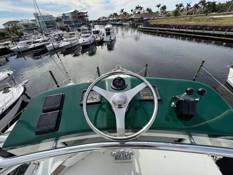Slide: The Image of Helm of 1999 Cabo 45 Express yacht overlooking marina with boats and palm trees. - 34