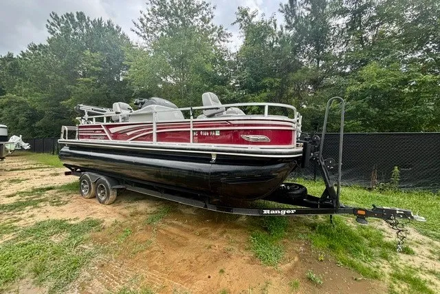 The Image of 2023 Ranger 223F pontoon boat on trailer, parked outdoors with trees in background. - 0