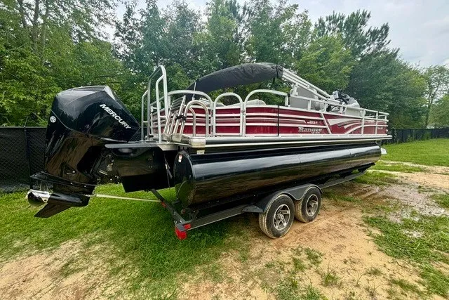 Slide: The Image of 2023 Ranger 223F pontoon boat on trailer, parked on grassy area with trees in background. - 2