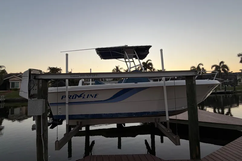 Slide: The Image of 1995 Pro-Line 21 Sport boat on lift at sunset, with palm trees in background. - 21