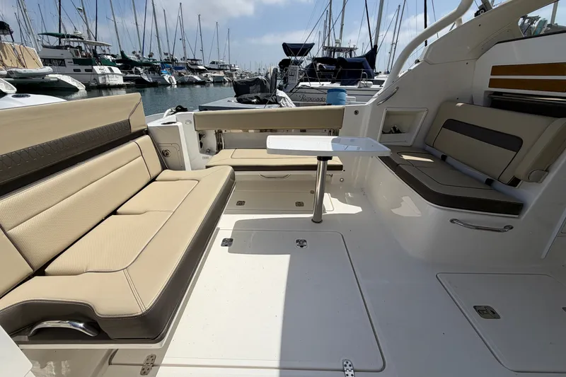Slide: The Image of 2019 Pursuit DC 365 Dual Console boat interior with beige seating and table, docked at marina. - 14