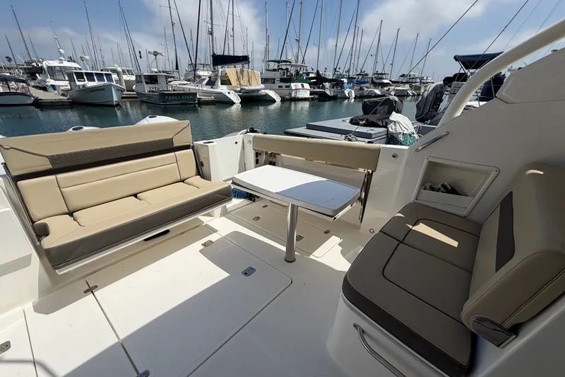 Slide: The Image of 2019 Pursuit DC 365 Dual Console boat interior with seating and table, docked at marina. - 13