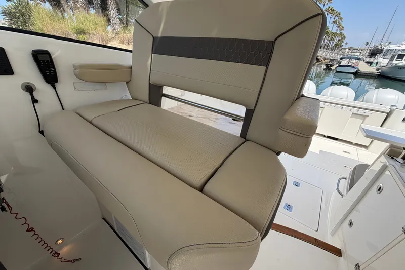 Slide: The Image of 2019 Pursuit DC 365 Dual Console boat interior with beige seating and marina view. - 37